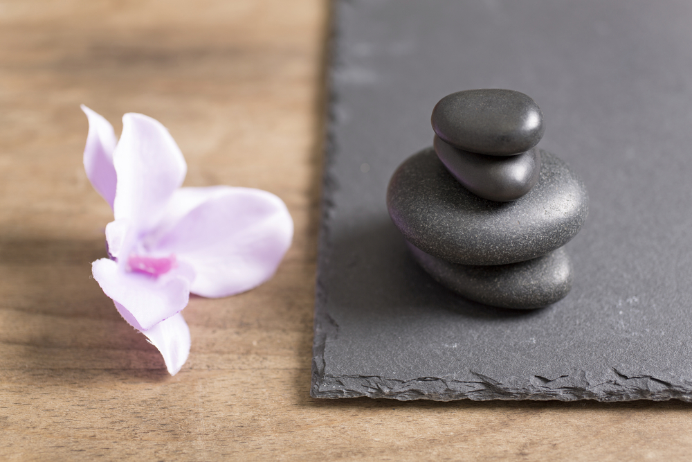 Pile of four spa stones with a fresh orchid flower next to it on a slate tray